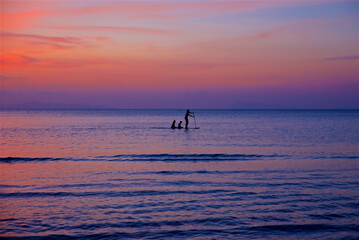 a woman and children swim on the sea on a board with a paddle, beautiful sunset and dawn on the island of Koh Samui in Thailand, time for meditation and relaxation, the sun is behind the horizon