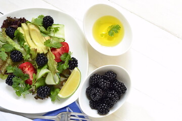 Avocado, blackberry, fresh herbs, сucumber and tomato salad with lime dressing,  top view, copy space