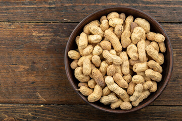 Unpeeled peanuts in a clay plate on a white wooden table. Space for text.