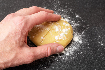 A female hand takes a raw dough for making bread, pie or pizza on a black background, close-up, top...