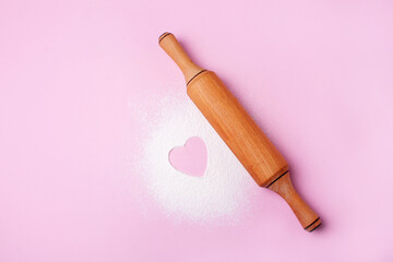 Rolling pin for baking and flour with heart on a pink background. Concept cook with love....
