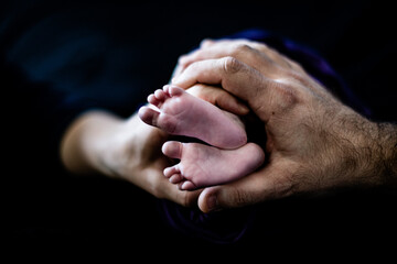 mom and dad hands around newborn baby feet