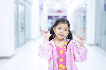 Asian child cute or kid girl lovely smile and make two finger hand to i love you symbol or Sarang-hae-yo for love valentine day or wedding and happy enjoy with wearing pink dress and coat or jacket