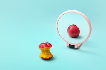 Bitten peach looking at its reflection in mirror on color background