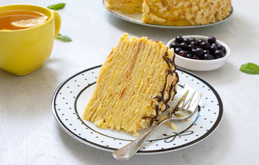 A piece of multilayer delicious vanilla cake on a plate and a cup of morning tea with lemon.