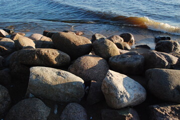 Large granite stones on the shores of the Gulf of Finland.
Autumn evening, the sun goes down. Near the water itself there are several large stones of various shapes and sizes. The stones are washed by