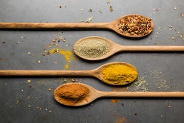various spices on wooden spoons, on stone table