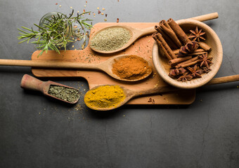 various spices on wooden spoons, on grey table with copy space