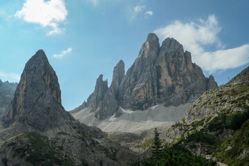 A panoramic view on Italian Dolomites. There are many high and sharp peak in front, with many landslides. Dangerous climbing. There are few trees and bushes on the side. Raw and unspoiled landscape