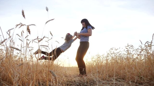 mom play with her daughter the park in wheat field. happy family people in the park concept. mom play is spinning daughter holding fun hands in wheat field. dream childhood happy family