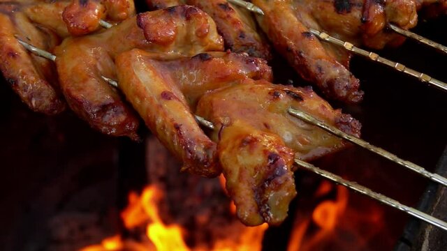 Close-up of delicious marinated chicken wings on the skewers frying above the open fire outdoors
