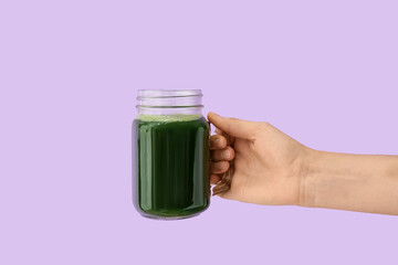 Hand with mason jar of vegetable juice on color background
