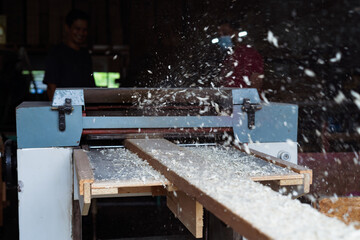 Carpenter working automated sanding machine for wood boards.