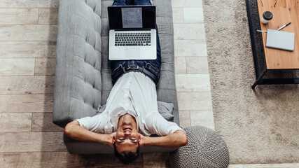 happy man with a laptop lying on the couch .