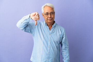 Middle age Brazilian man isolated on purple background showing thumb down with negative expression