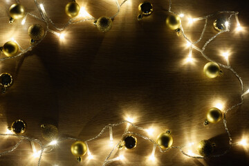 New year christmas frame from golden shiny and matte balls, christmas lights garland on light wood background with copy space