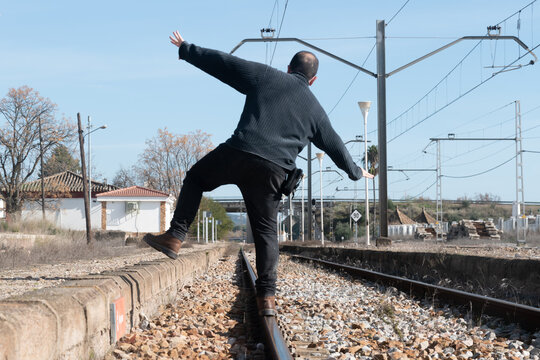 
Hombre de espaldas caminando sobre v&iacute;as de tren abandonadas , concepto de equilibrio Imagen inclinada
