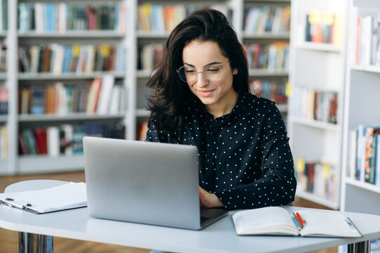 Busy Caucasian Young Woman, In Eyeglasses Is Sitting At The Desk While Remote Work From Home And Chatting Online Using A Laptop