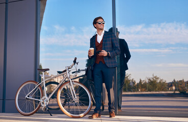 Cheerful businessman with bicycle and takeaway coffee