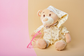 cute teddy bear and pink baby glasses on beige and pink background