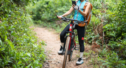 Fototapeta na wymiar Woman cyclist use smartphone when riding mountain bike on forest trail