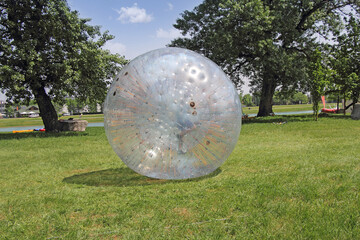 A boy walks in a large plastic ball on the green grass - 399237042