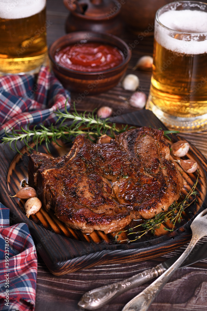 Wall mural Roasted  pork chop on the bone steak.
The meat is served on a wooden plate with rosemary and thyme, fried garlic.