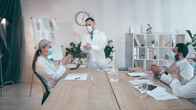 chief physician with colleagues in medical masks applauding during conference