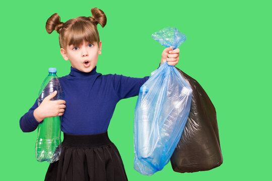 Little ecologist girl with confused funny face holding trash bags with plastic bottles isolated on green background