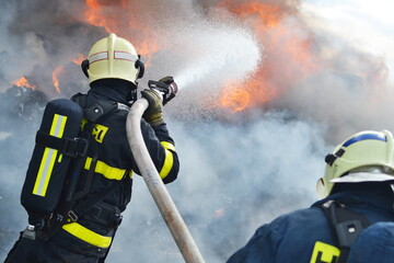 A fireman extinguishes huge landfill fire with flames and smoke in the background