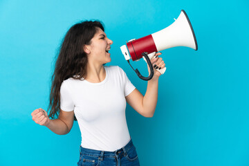 Teenager Russian girl isolated on blue background shouting through a megaphone to announce...