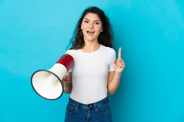 Teenager Russian girl isolated on blue background holding a megaphone and pointing up a great idea