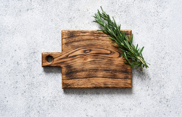 Cutting board with rosemary on a light concrete background.