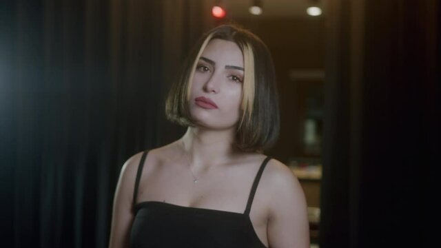 Beautiful girl with wind blowing her short hair. Young beautiful and attractive woman in a black dress poses serious looking at the camera in a modern space.