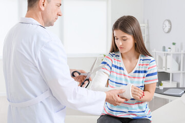 Doctor going to remove plaster from young woman's arm in clinic