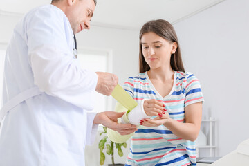 Fototapeta premium Young woman with broken arm visiting doctor in clinic
