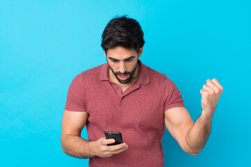 Young handsome man with beard over isolated blue background surprised and sending a message