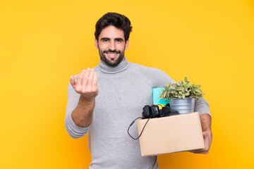 Young handsome man with beard making a move while picking up a box full of things over isolated...