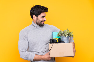 Young handsome man with beard making a move while picking up a box full of things over isolated...