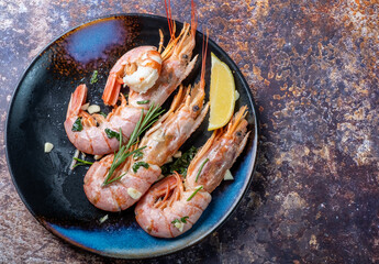 Cooked shrimps with garlic and herbs in a dark plate. Top view.