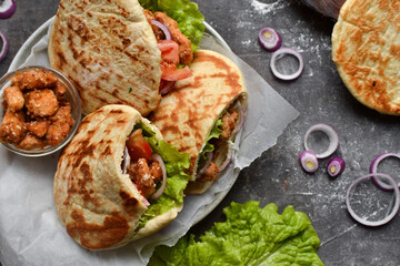 Lavash salad with fried chicken and vegetables. Pita with chicken nuggets, tomatoes, red onions and lettuce and sauce. Healthy fast food. Top view. Dark background.