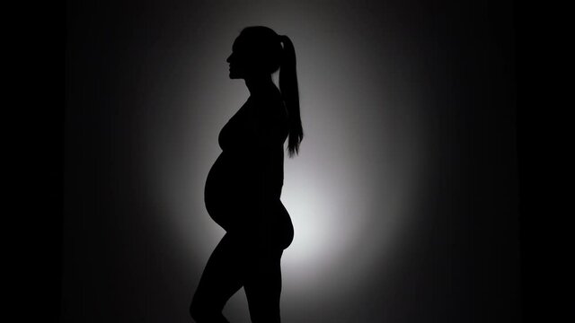 a silhouette of a pregnant woman dancing and showing her biceps on a black background