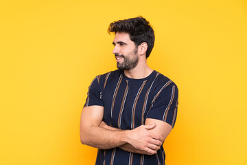 Young handsome man with beard over isolated yellow background looking to the side