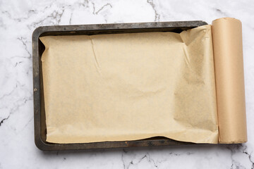 rectangular metal baking sheet and roll of brown parchment paper on white background