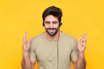 Telemarketer man working with a headset over isolated yellow background laughing