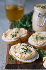 Homemade pate, spread or mousse in glass jar with sliced bread and herbs, light concrete background.
