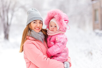 beautiful young smiling woman in pink coat holds a one-year-old baby girl. people ziomy in stylish clothes