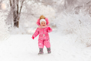 Baby girl in pink winter jumpsuit stands in the snow