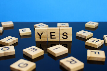 Yes word made of wooden letters on a mirror surface on a blue background