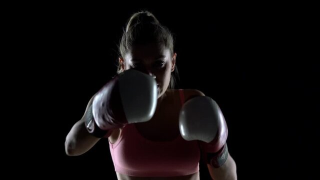 slow motion of the silhouette of a young woman training with boxing gloves. strikes in the direction of the camera